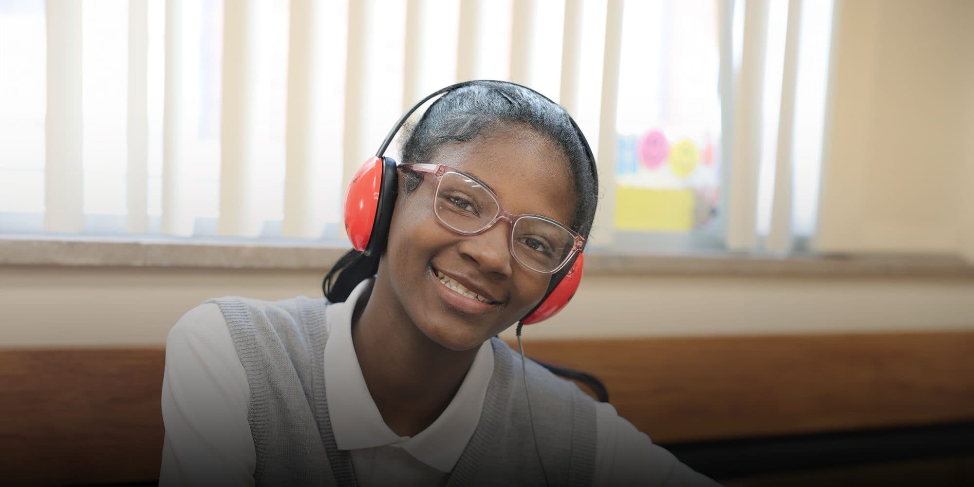Smiling student wearing red headphones and glasses at her desk.